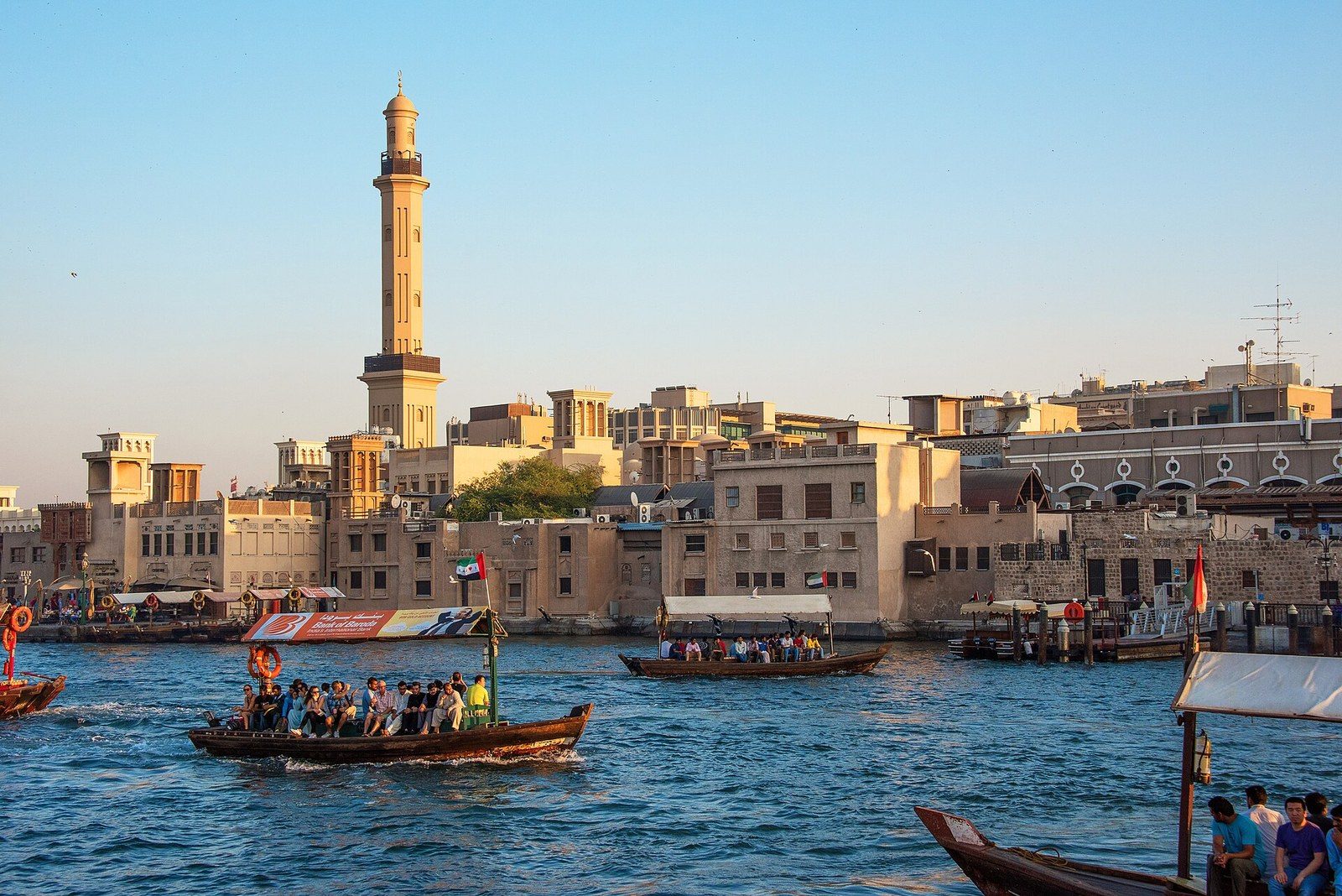 What to do in Dubai in one day: wooden abras with passengers cross the Creek below a minaret and old houses